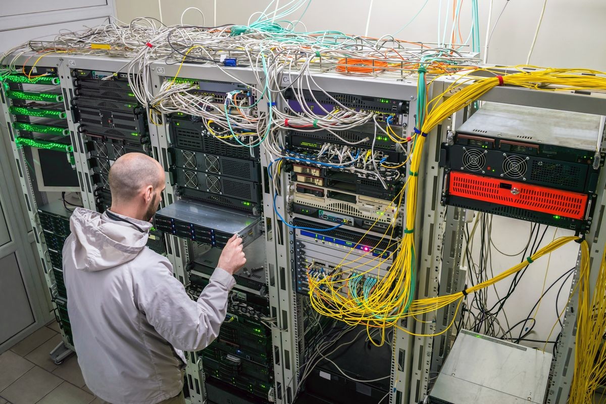 A man installs new equipment in the computer rack of the server room. The system administrator updates the hardware of the datacenter. Technical work on the site. View from above.