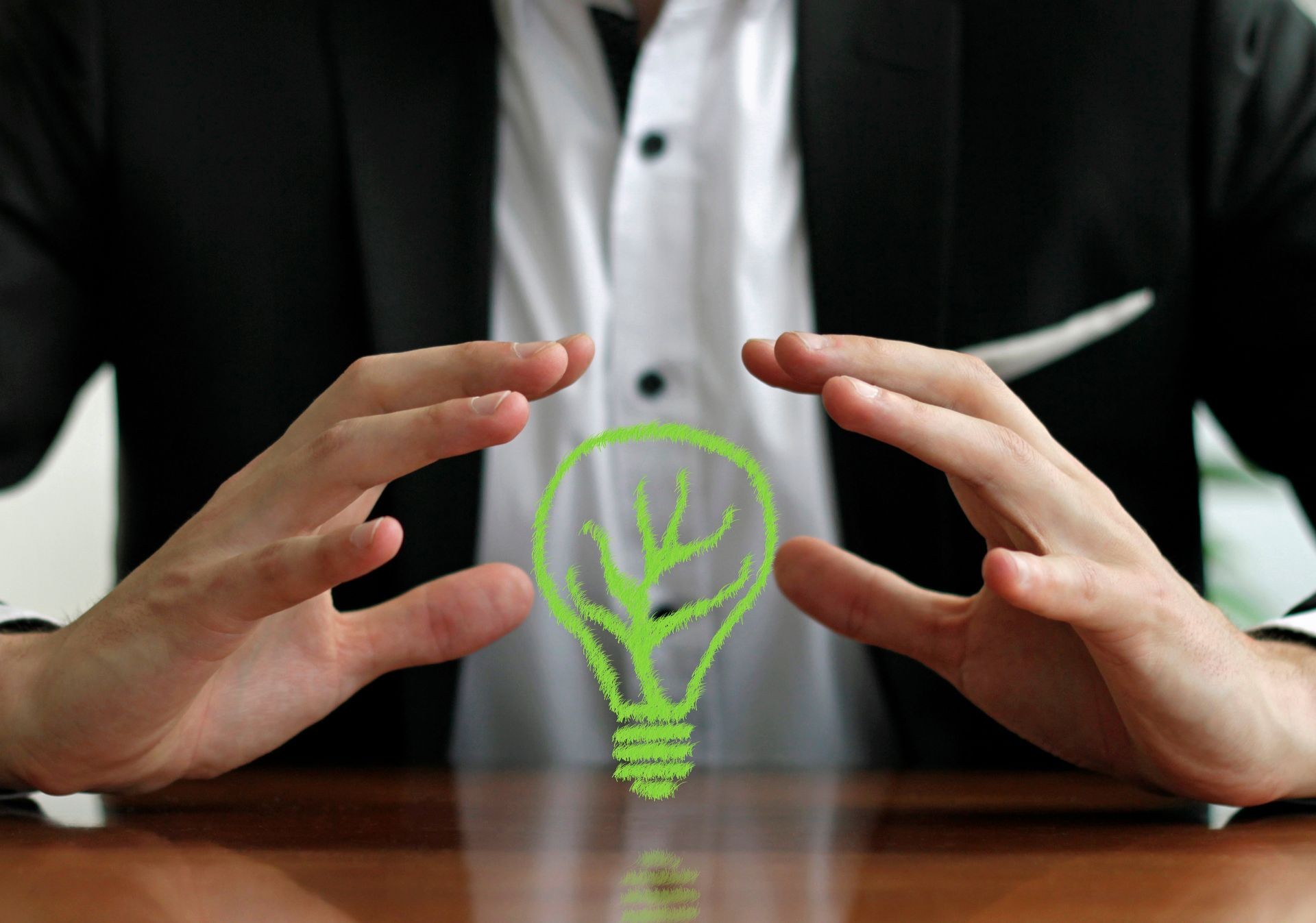 Protecting sustainable energy - businessman with hands around a green light bulb