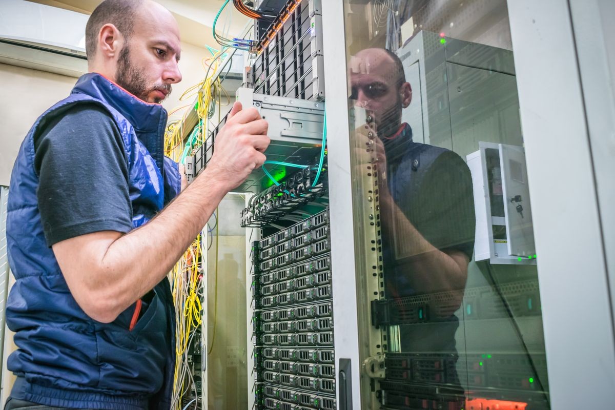 A man works in a server room. Technician repairs the central router. System administrator installs a new server in a modern data center. The engineer replaces the computer equipment in the cabinet.